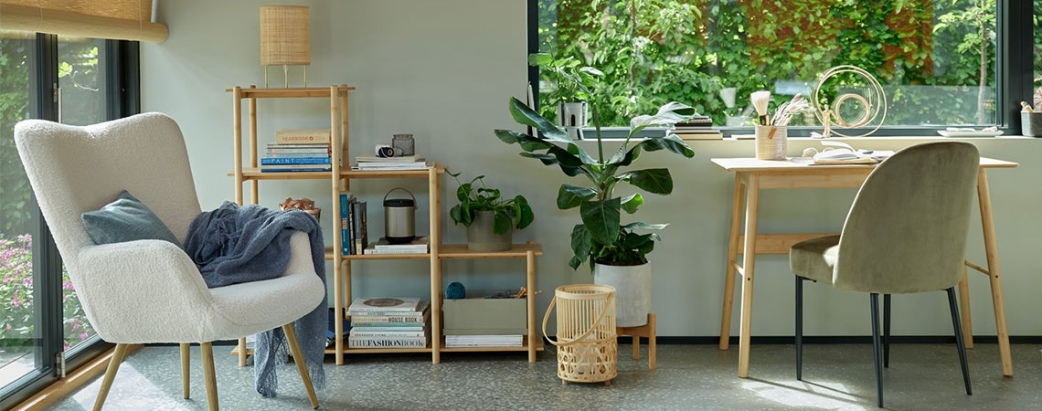 Sillón gris junto a una ventana y un separador de ambientes de bambú al fondo. Farol de bambú en el suelo junto a un escritorio de bambú y una silla de comedor verde oliva. 