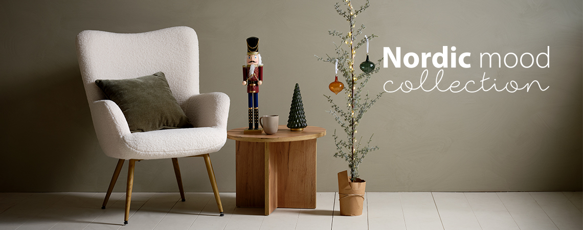 Sillón con un cojín, mesa de centro con una figura navideña y un esbelto árbol de Navidad decorado con chucherías de cristal