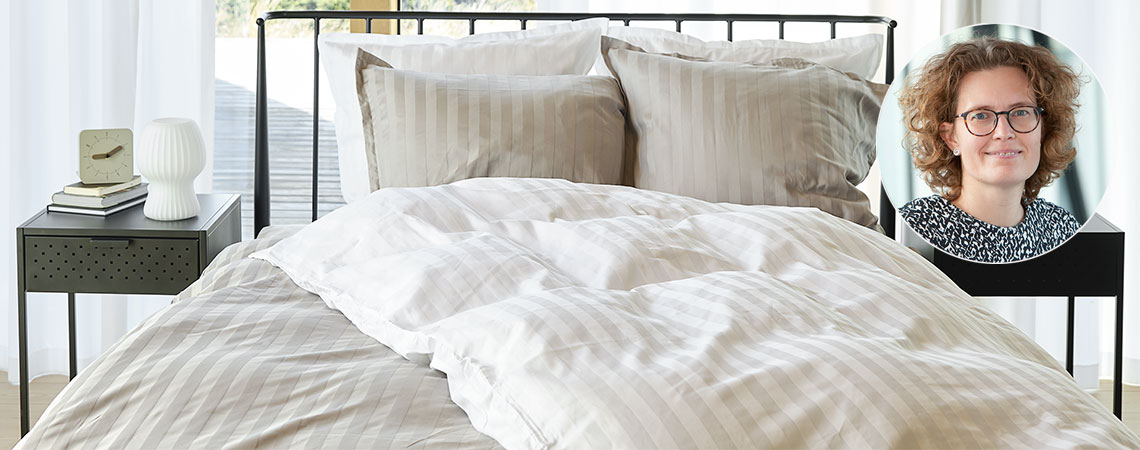 Dormitorio con cama, edredones y almohadas, cubierto con ropa de cama a rayas e inserto de Berit Christiansen