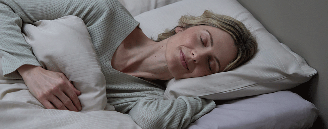 Mujer durmiendo de lado en la cama con una almohada blanca y un relleno nórdico