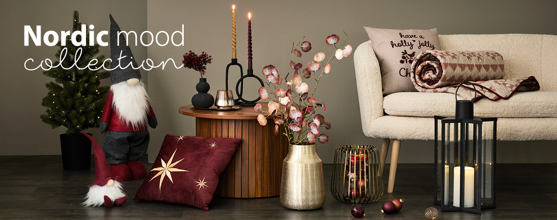 Duendes navideños, cojines, jarrón dorado con flores artificiales, candelabro dorado y farol negro frente a un sofá blanco