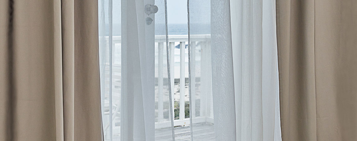 Vista a un balcón a través de una puerta abierta con cortinas ondeantes