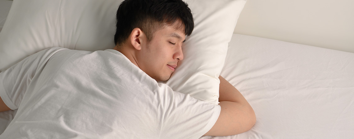 Hombre durmiendo plácidamente en la cama con almohada blanca y topper blanco