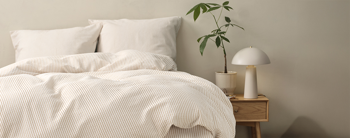 Cama con ropa de cama a rayas en dormitorio con mesita de noche y lámpara