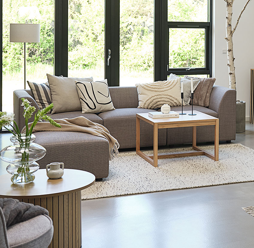 Mesa de centro minimalista de roble en un luminoso salón con un gran sofá y cojines decorativos 