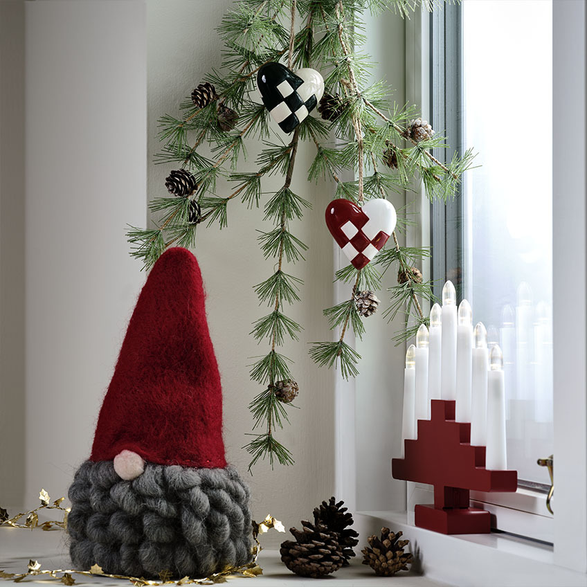 Duende navideño escandinavo con barba gris en una repisa de ventana decorada.