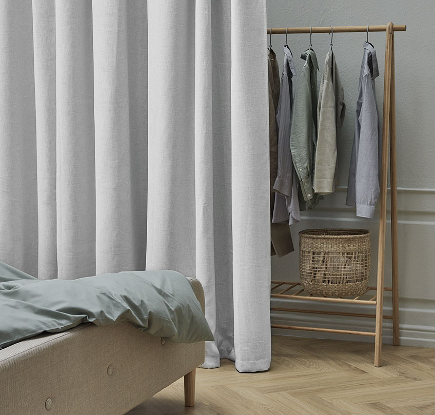 Cortina beige delante de una barra de colgar separa una zona de dormitorio de una zona de armario