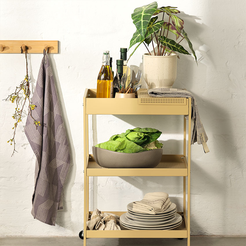 Decoración de mesa en el carrito ELLERUP en una cocina con platos, un bol grande, cubertería y una planta artificial