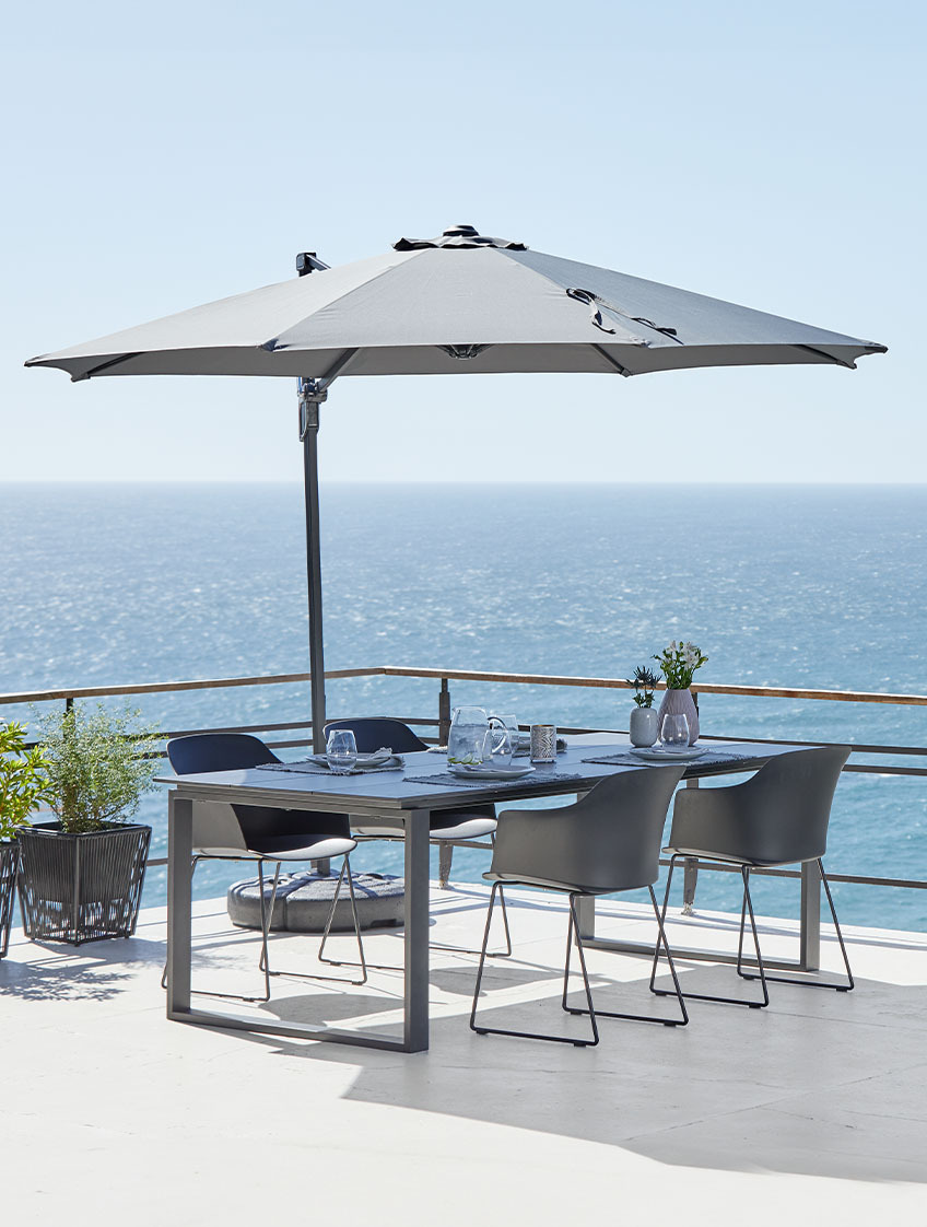 Gran sombrilla colgante y mesa de jardín y sillas en una terraza con vistas al mar 