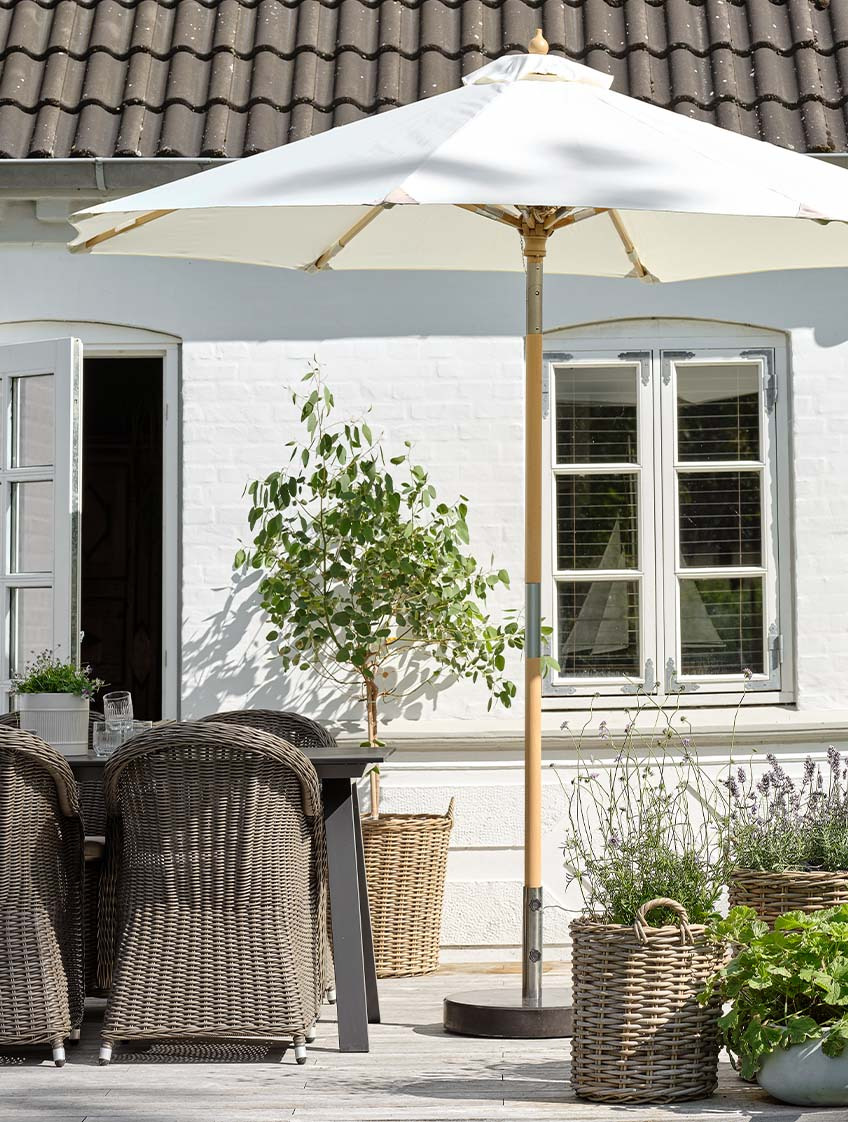 Sombrilla de jardín clásica, en color blanco crudo, en una terraza con una mesa de jardín y sillas de jardín 