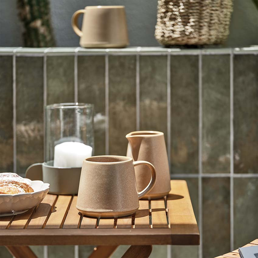 Taza de café y jarra de leche en una mesa de jardín pequeña y de madera al sol 