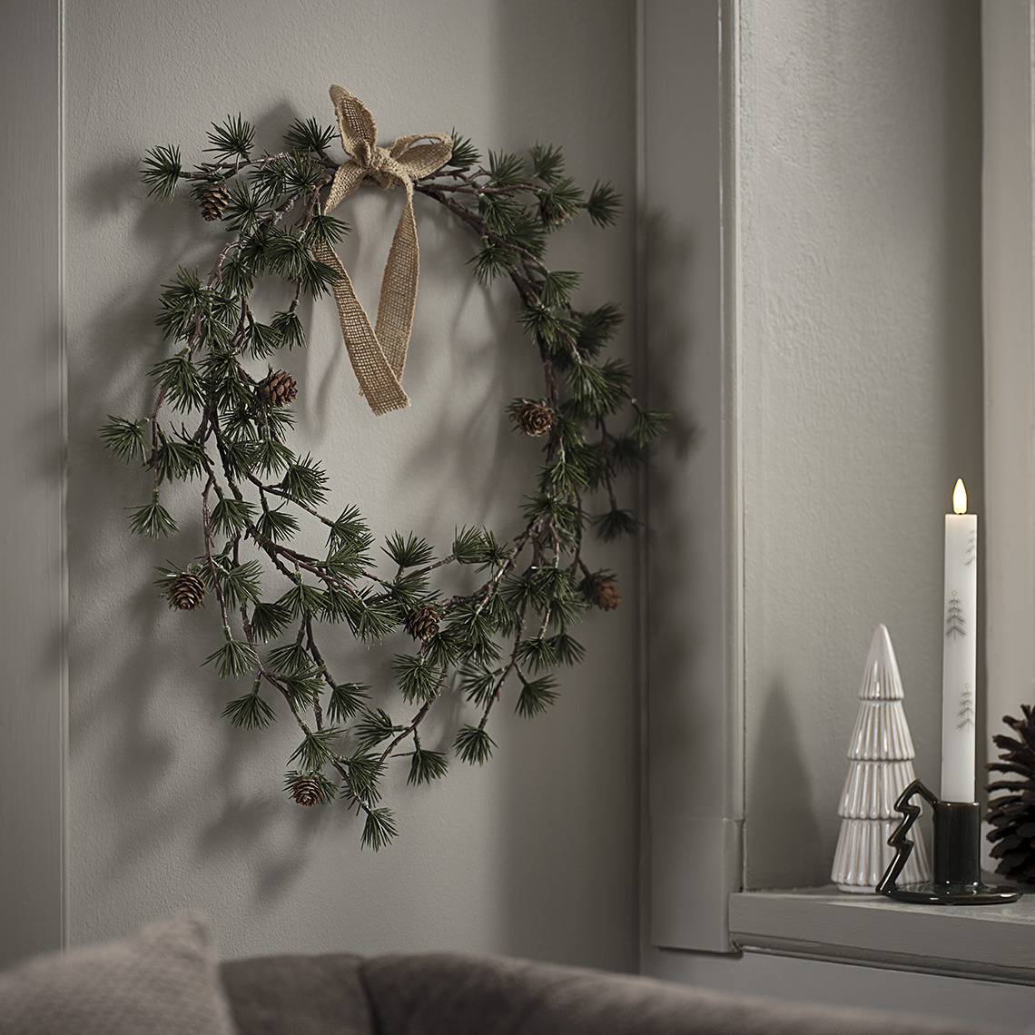 Corona de Navidad junto a una cornisa con un árbol de Navidad decorativo y una vela de Navidad