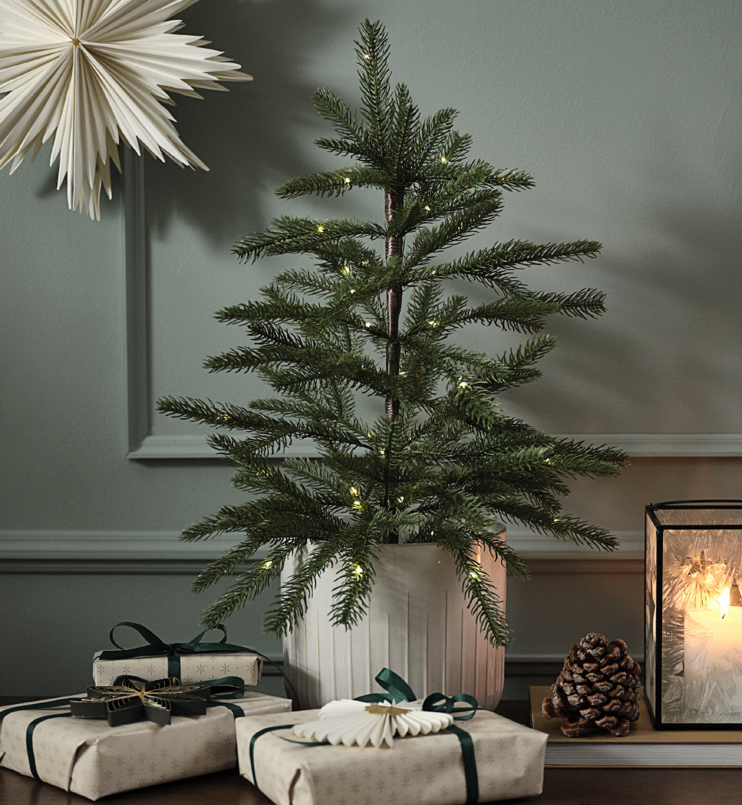 Árbol de Navidad artificial en una maceta con luces y una estrella de papel en la pared 