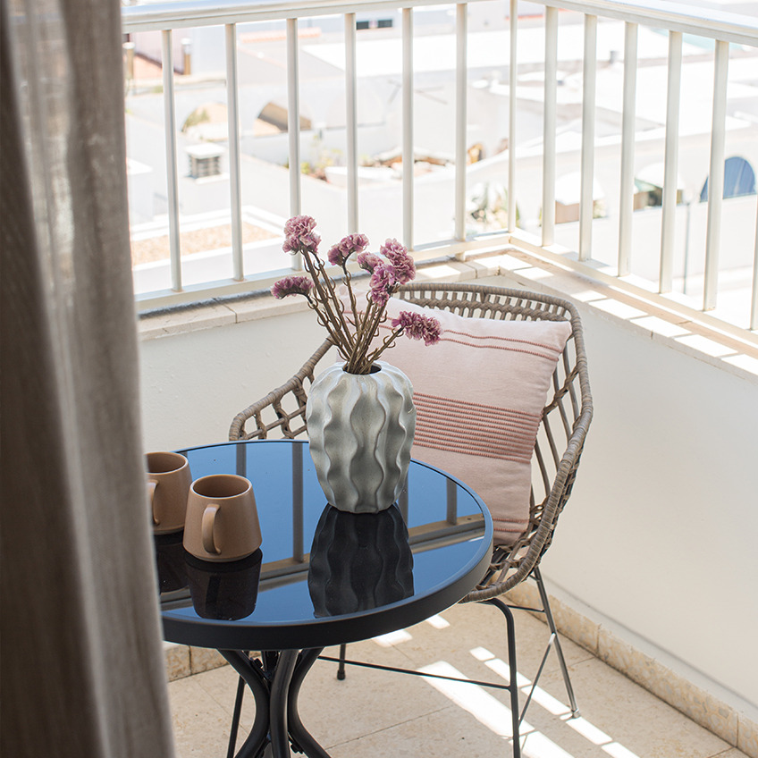 Zona de balcón con silla, mesa y decoración.