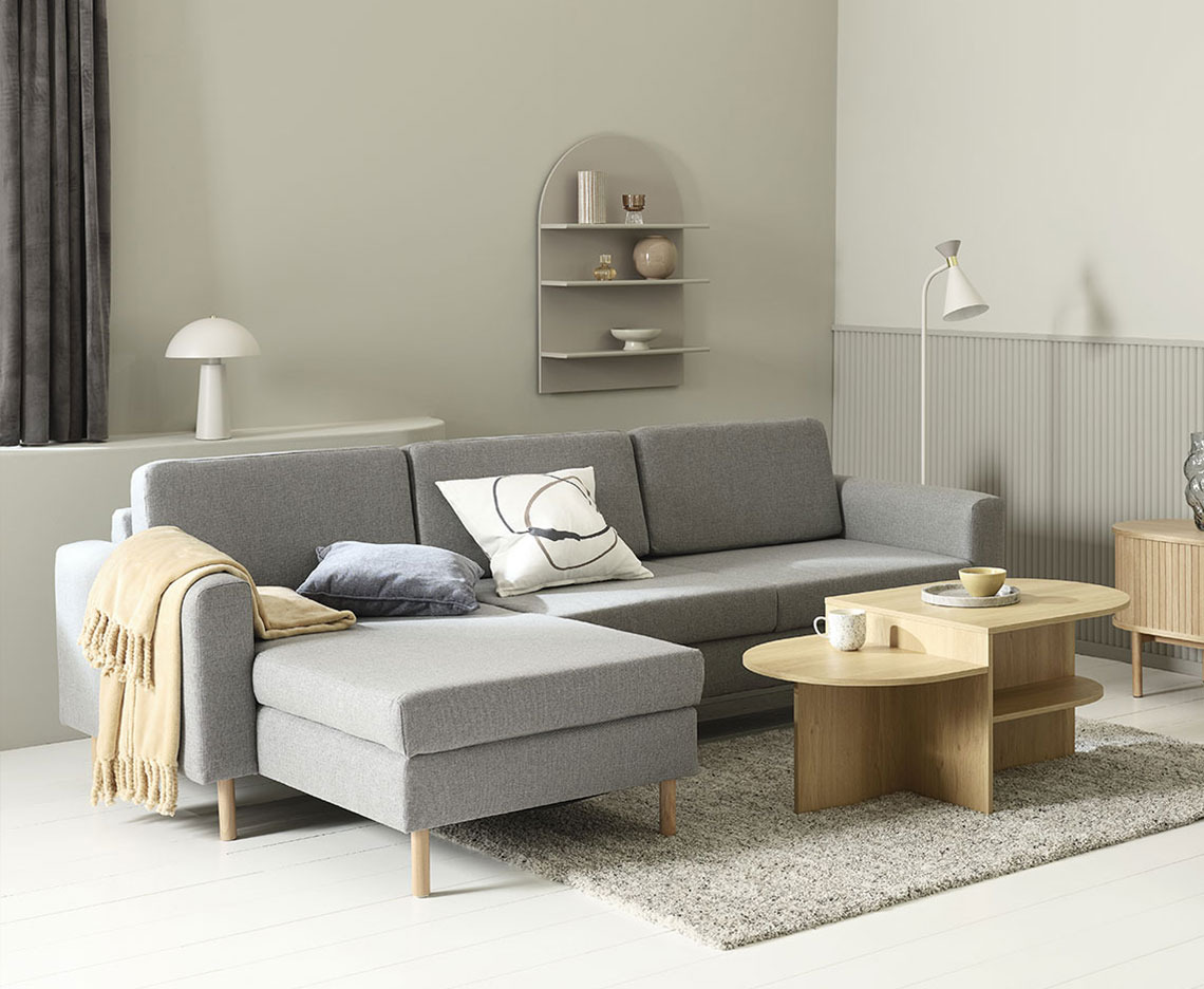 Sofá con chaise longue gris en un salón con mesa de centro, lámparas y decoración 