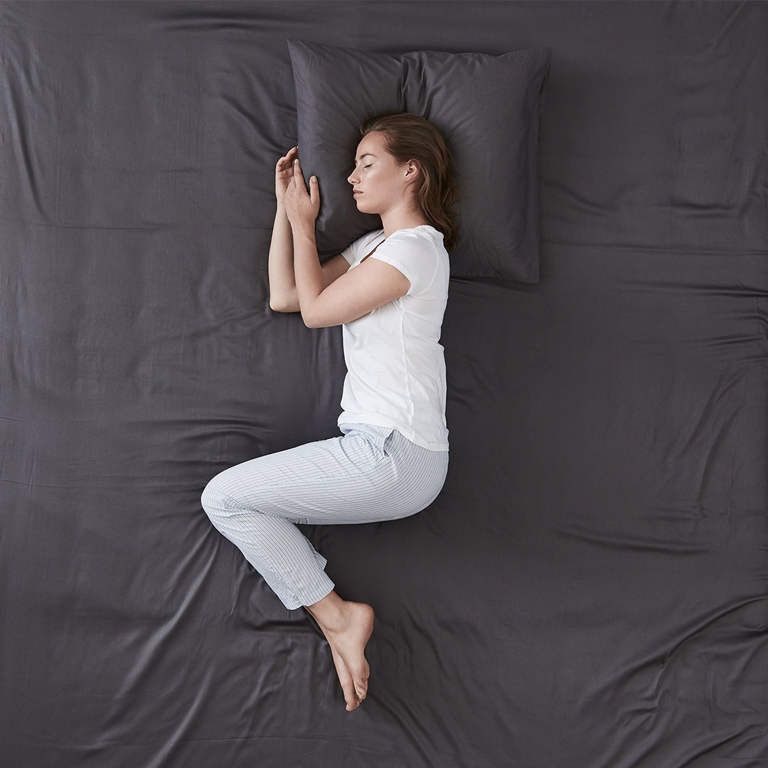 Mujer durmiendo de lado en una cama con ropa de cama gris oscuro