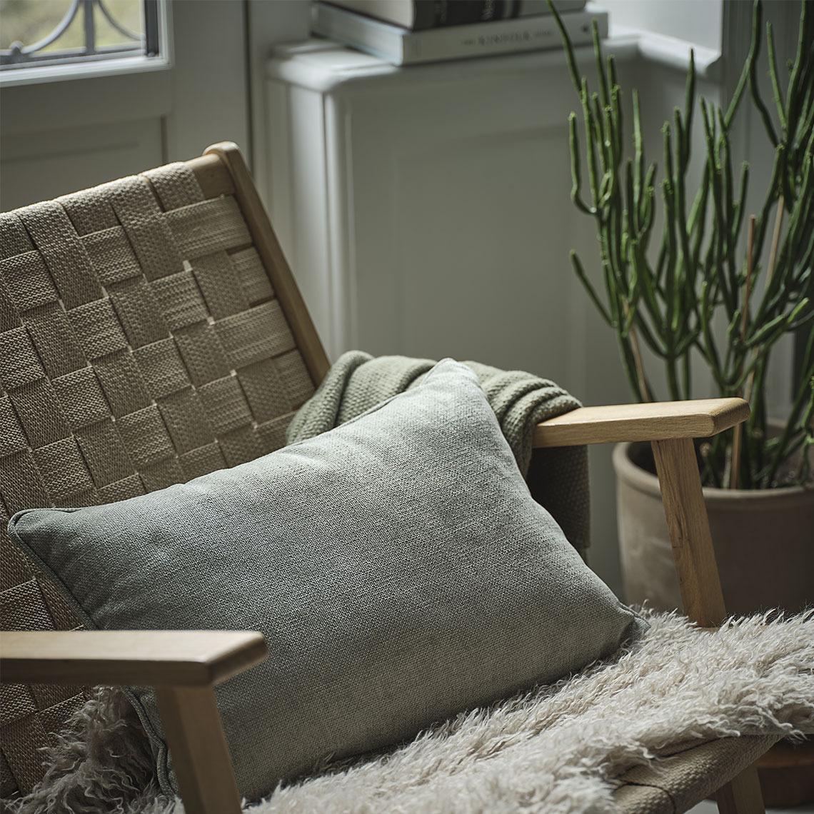 Cojín verde en una silla con una manta verde y una piel de cordero beige