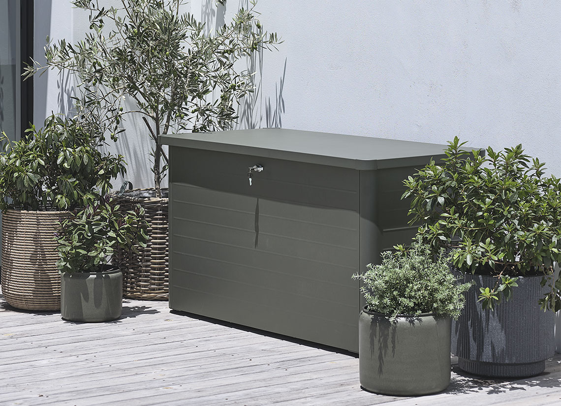 Baúl para cojines de color gris en una terraza con plantas y macetas