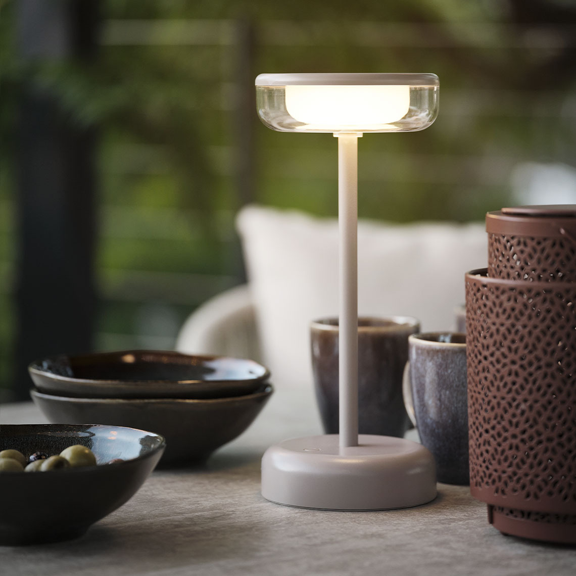 Lámpara de mesa exterior HUMLEBI a pilas Lámpara de mesa a pilas sobre una mesa de jardín con tazones y tazas