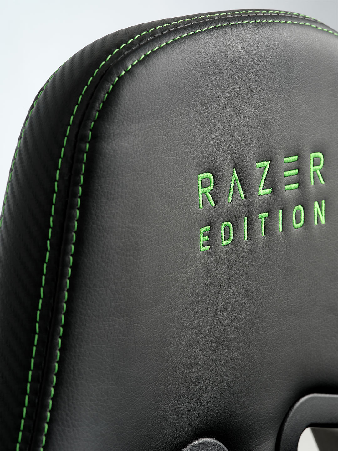 Primer plano de una silla gaming Racer negra con costuras verdes y "RAZER EDITION" bordado en verde en el respaldo.
