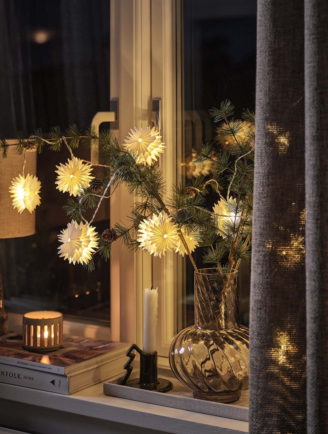Guirnalda de luces con forma de estrella en unas ramas de pino en un jarrón que ilumina una ventana de noche 