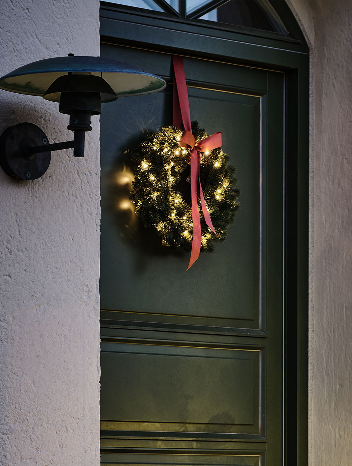Corona de Navidad de exterior encendida con pequeñas luces, colgada en una puerta