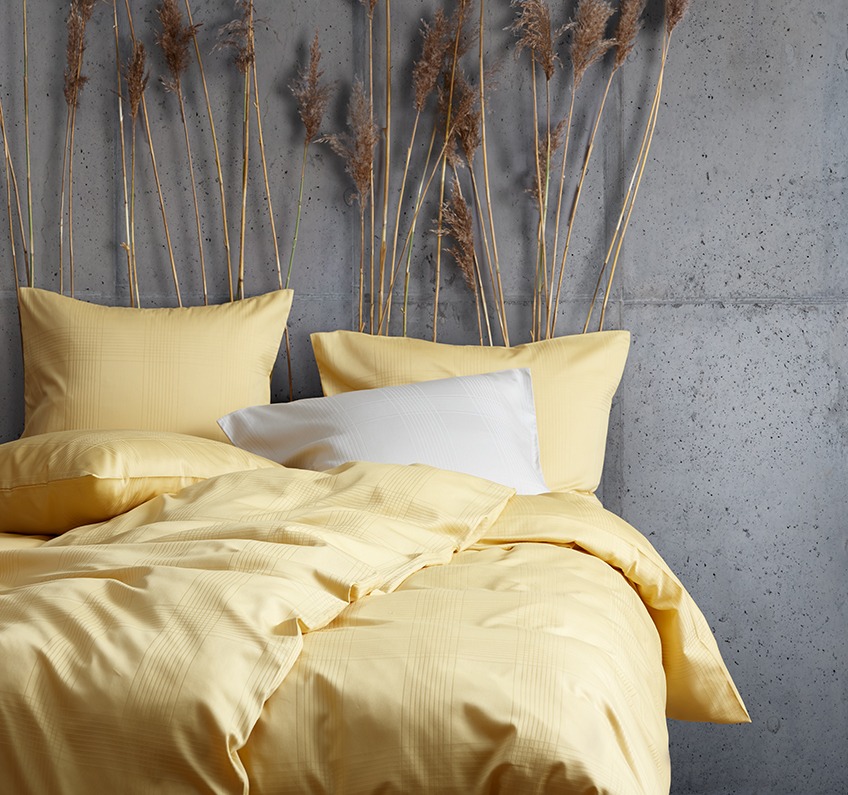 Yellow bed linen out of 51% recycled polyester and 49% cotton sateen in a bedroom with concrete walls 