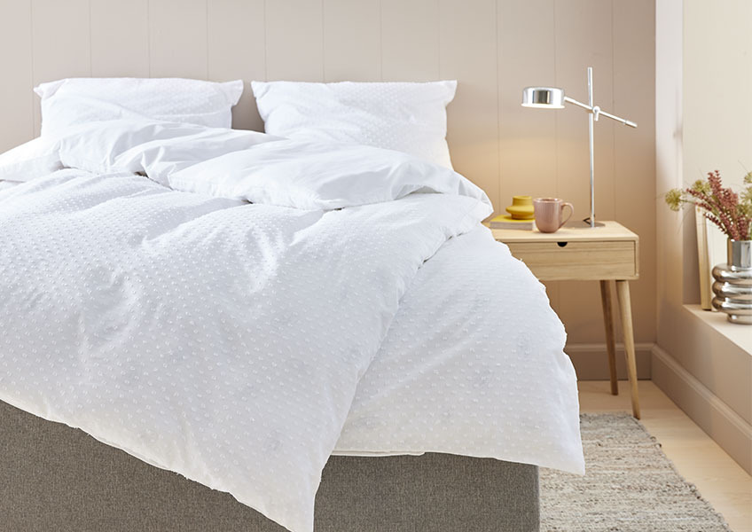 Bed with a white dotted duvet cover set in a bedroom with bedside table and chrome table lamp