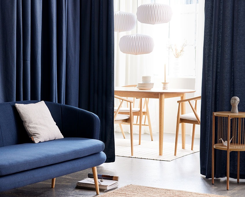 Blue curtain behind a sofa separates a living area from a dining area 