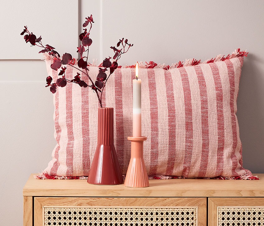 Striped cushion behind red vase and candlestick with striped candle  