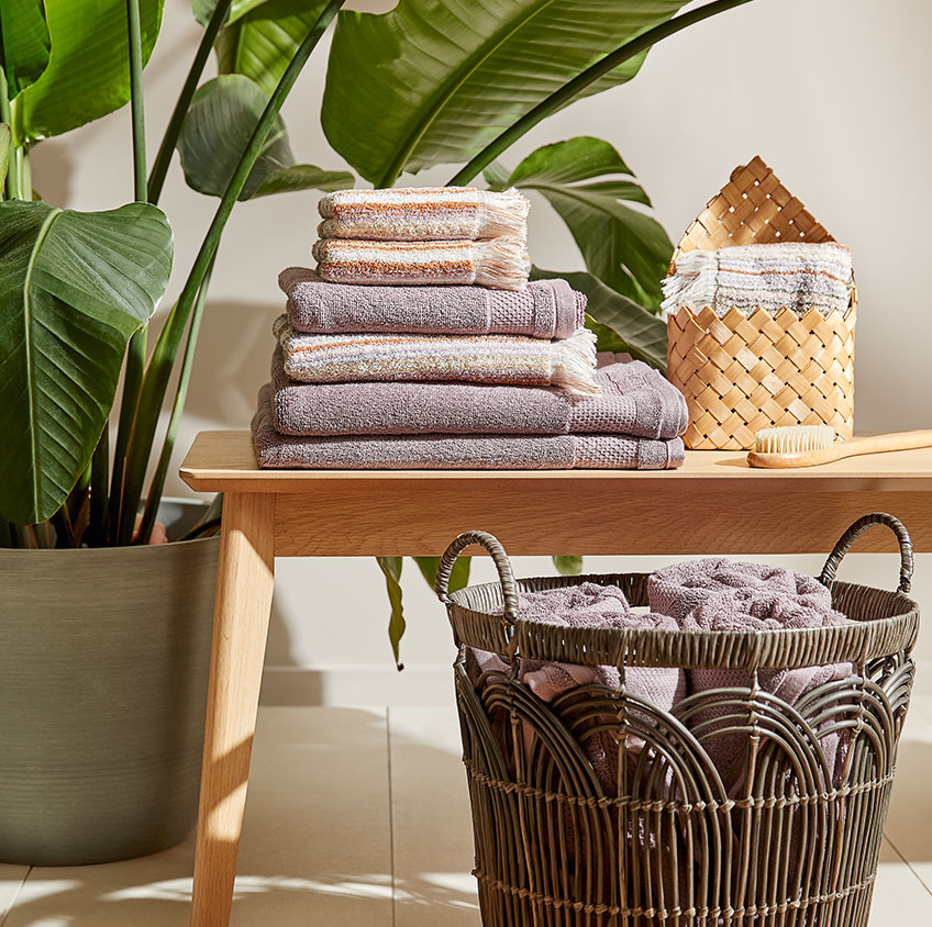 Toallas de algodón y cestas de rafia encima de un banco en el baño. 
