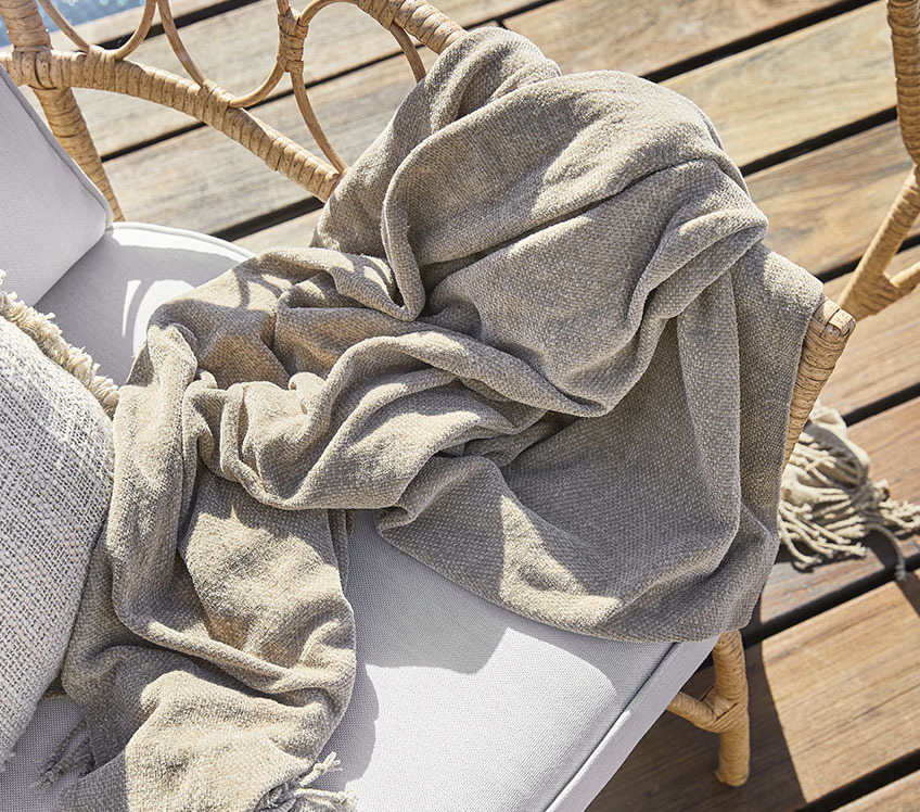 Lounge chair with a khaki throw on a wooden patio  