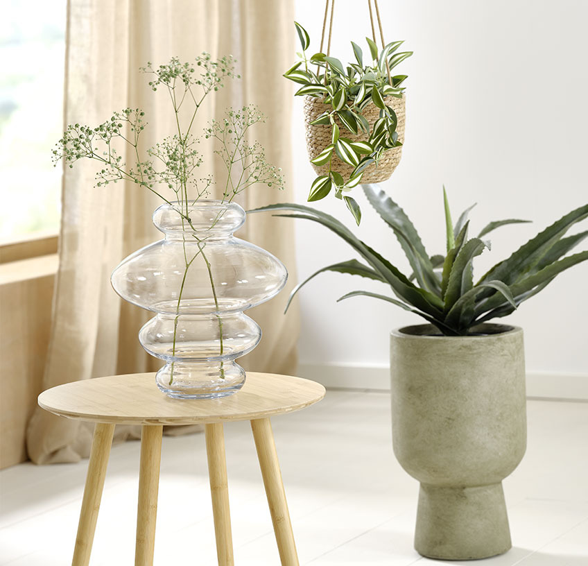 Jarrón de cristal sobre una mesa auxiliar, maceta colgante y maceta verde con plantas artificiales