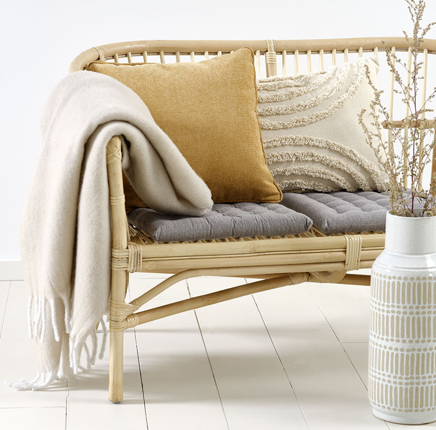 Sofá LISELEJE con cojín GRAVMYRT beige, cojín HORNFIOL amarillo y manta TUSENFRYD Sofá de ratán con cojines beige y amarillo y manta beige.