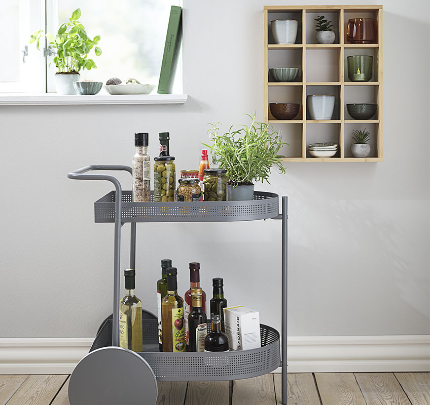 Carrito gris decorado con artículos de cocina y un estante de pared con tazas y tazones