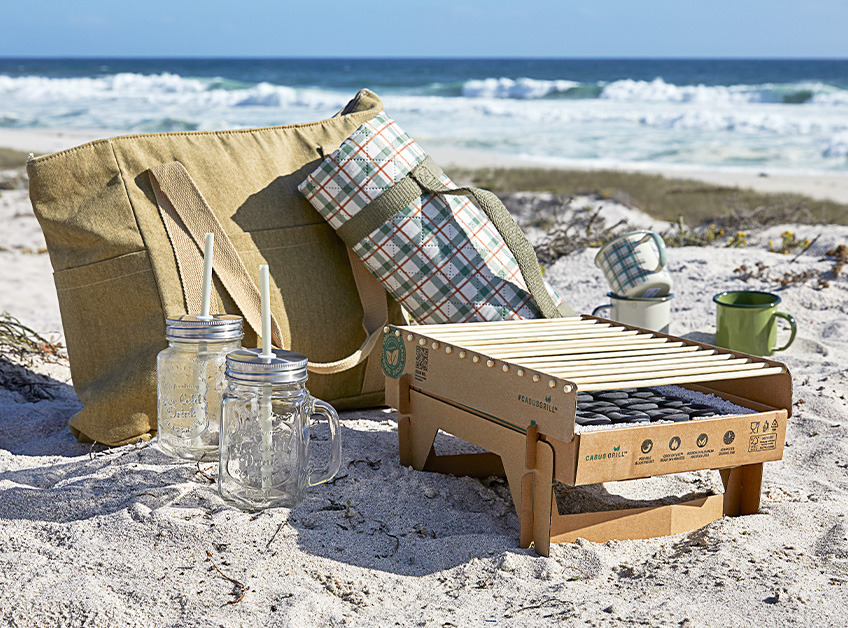 Barbacoa desechable eco-friendly, bolsa y manta de picnic y vasos y tazas en la playa