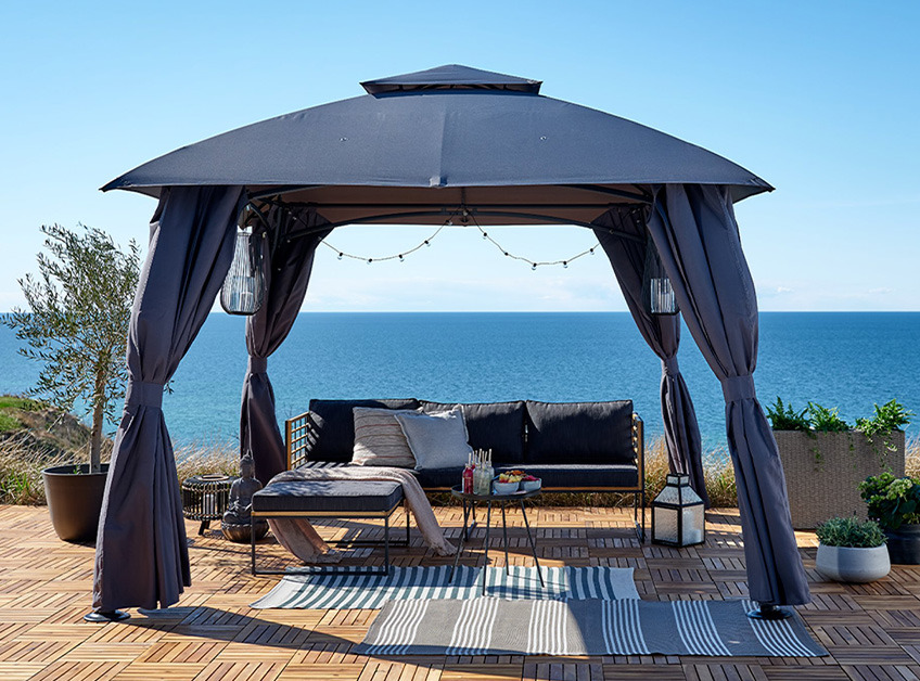 Cenador SANKT HANS y sofa de jardín UGILT Cenador gris con mobiliario de jardín y elementos decorativos con vistas al mar