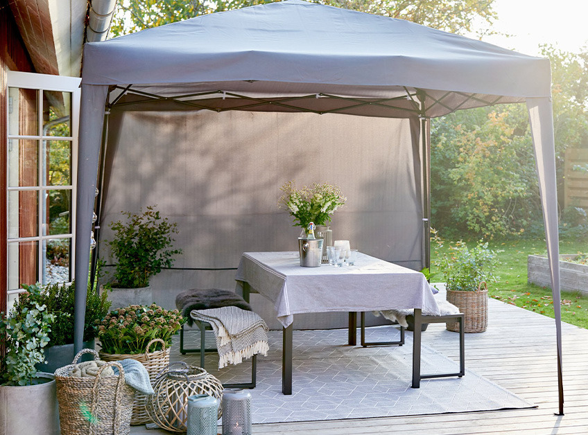 Cenador gris con un conjunto de mesa y bancos con elementos decorativos en una terraza 