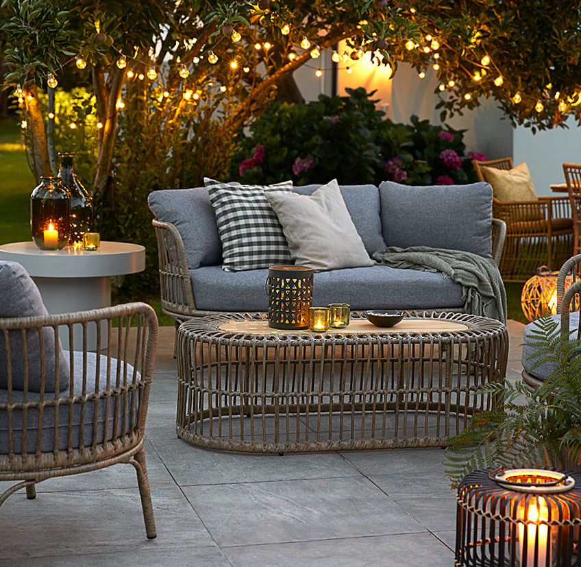 Cómodos muebles de salón en el patio con luces de cuerda, lámparas de pilas y farolillos con velas y candelitas